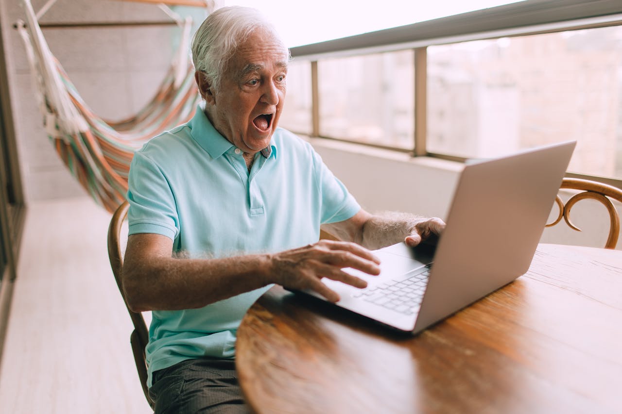 Elderly man in a hammock chair surprised while using laptop indoors. Bright and candid moment.
