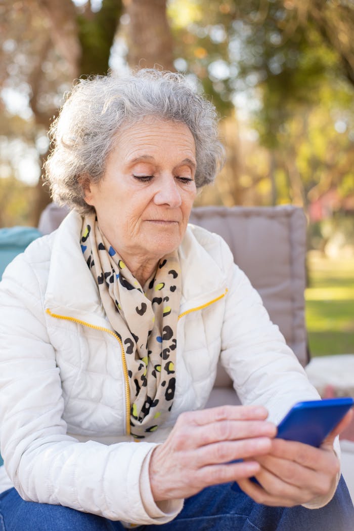 Senior woman with gray hair using a smartphone outdoors during springtime in Portugal.