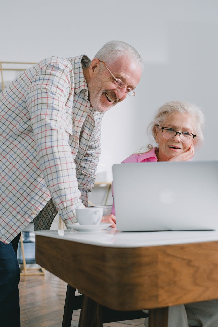 Senior couple smiling and interacting with a laptop at home, enjoying technology together.